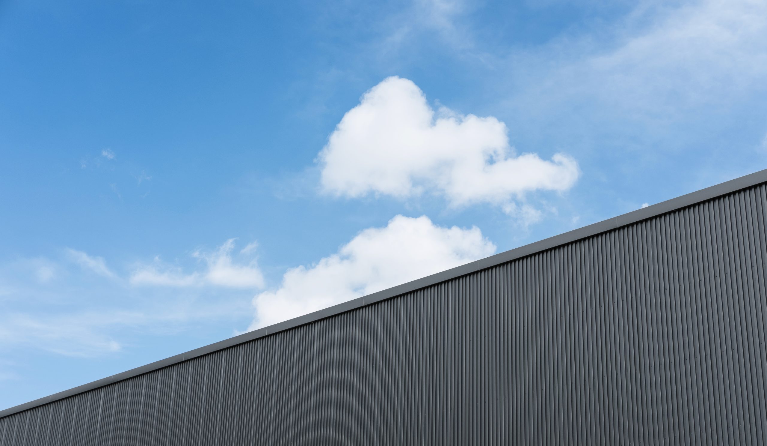 Corrugated factory industry wall on blue sky with clouds